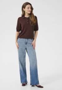 Polo a maniche corte marrone con bottoni, abbinato a jeans larghi azzurri chiari e scarpe marroni scure. Design semplice, look casual.