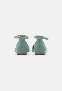 Mocasines de ante en color verde azulado con cierre trasero, tirante en el tobillo y tacón bajo. El diseño incluye recortes en los lados para mayor transpirabilidad.