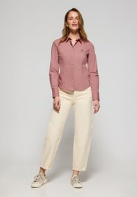 Camicia a maniche lunghe con bottoni di colore rosa polveroso, abbinata a pantaloni larghi color crema e sneaker beige. Design semplice con colletto classico.