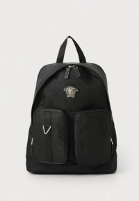 Mochila preta em nylon com dois bolsos frontais com fecho de correr, pega superior e alças ajustáveis. Apresenta um emblema proeminente da Medusa na parte frontal.