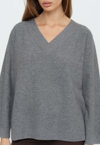 Maglione grigio a scollo a V realizzato in tessuto morbido con maniche lunghe e vestibilità ampia. Presenta una texture sottile e piccole scintille su tutta la superficie.