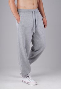 Man wearing grey sweatpants with drawstring and white sneakers, standing with hands in pockets against a neutral background.