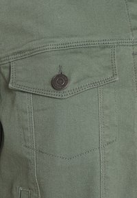 Chaqueta de mezclilla verde con un bolsillo en el pecho, con un botón de metal, costuras de contraste y una tela texturizada.