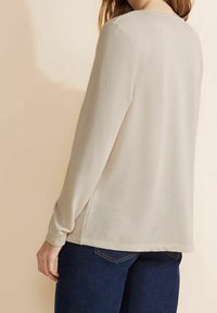 Ljusbeige stickad tröja med rund halsringning och långa ärmar, med en lös passform och ribbade muddar, kombinerad med mörkblå jeans.