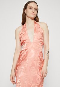 Robe à col halter en satin corail doux avec motif de feuilles. Dotée d'un décolleté en V profond et d'une jupe fluide, mettant en valeur une texture lisse.