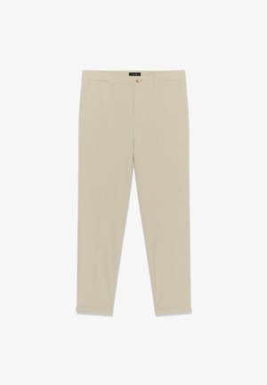 Béžové nohavice úzkeho strihu s pútkami na opasok, prednými vreckami, zapínaním na gombíky a zastrčenými lemami, uložené na bielom pozadí.