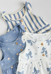 Three baby dresses: blue with hearts, striped blue and cream, and white with navy bow patterns. All have button details and shoulder ties.