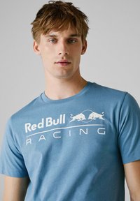 Lyseblå bomulds T-shirt med "Red Bull Racing" tekst i hvid, korte ærmer, rund hals og en glat overflade.