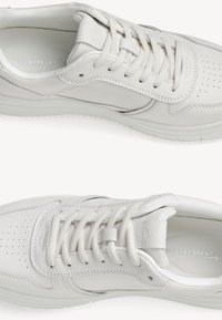 Białe skórzane sneakersy o gładkiej fakturze, perforowanym palcu, okrągłych sznurówkach i delikatnych akcentach projektowych po bokach.