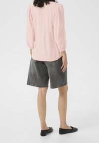 Lys rosa, tekstureret bluse med trekvartærmer, parret med løse, mørkegrå denimshorts og sorte flade sko.