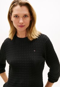 Schwarzer Strickpullover mit strukturiertem Muster, rundem Ausschnitt und Dreiviertelärmeln. Verfügt über ein kleines Markenlogo auf der Brust.