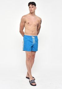 Pantaloni da bagno blu con vita regolabile, caratterizzati da strisce verticali a contrasto sui lati. Tessuto liscio e leggero.