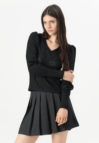 Maglione nero a maglia con scollo a V e maniche a sbuffo, abbinato a una gonna plissettata di colore grigio antracite. Il tessuto strutturato aggiunge profondità.