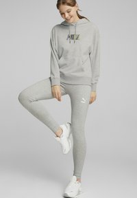 Grå hoodie med "PUMA"-logotyp, tillsammans med matchande grå tights som har en vit logotyp. Vita sportskor fulländar klädseln.