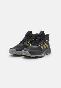 Zapatillas deportivas negras con parte superior de malla, acentos dorados, cuello acolchado y suela texturizada gris. Presentan rayas decorativas en los laterales y cordones.