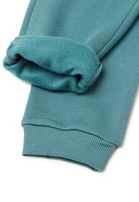 Tealowe dresy mają miękki, podwójnie złożony mankiet z prążkowanym wykończeniem. Materiał ma gładką fakturę i lekko szczotkowane wnętrze dla zapewnienia ciepła.