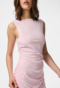 Ružičasta haljina bez rukava s cvjetnim vezom, nabranim dizajnom i gladakom, mekom teksturom. Tkanina je lagana i prilagođava se tijelu.