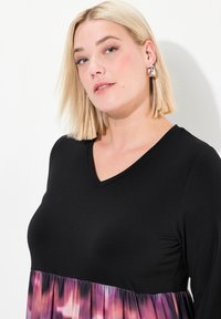 Top nero a scollo a V con maniche lunghe, caratterizzato da un fondo plissettato multicolore nei toni del viola e del rosa. Tessuto liscio e leggero.
