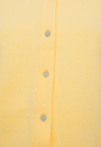 Gros plan sur un tissu tricoté jaune avec trois boutons ronds bleu clair alignés verticalement.