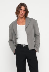Grey blazer with a structured design, notched lapels, and two buttons; paired with a white tank top and black trousers.