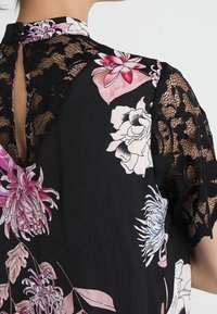 Vestido negro con flores que presenta un espalda de encaje y mangas cortas, con flores en tonos rosa y blanco. El detalle de ojal en el escote añade interés.