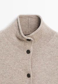 Světlý béžový pletený svetr s vysokým límcem, dvěma černými knoflíky a žebrovaným vzorem podél krku a manžet. Měkká textura.