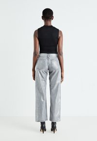 Top sin mangas negro, pantalones anchos metálicos grises con bolsillos laterales y bolsillos traseros, usados con botas de tacón negras hasta el tobillo.