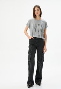 Grå T-shirt med korteærmer og et vertikalt mønster, parret med sorte cargo-bukser med vide ben og store sidelommer, samt sorte spidse sko.