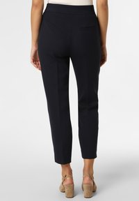 Pantaloni blu navy con un design aderente, vita testurizzata, gambe slim e una tasca posteriore singola. Indossati con scarpe beige con tacco a blocco.