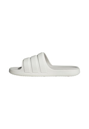 Sandalia blanca tipo slip-on hecha de goma suave, con tres franjas horizontales prominentes en la parte superior, que presenta una suela plana y una plantilla texturizada.