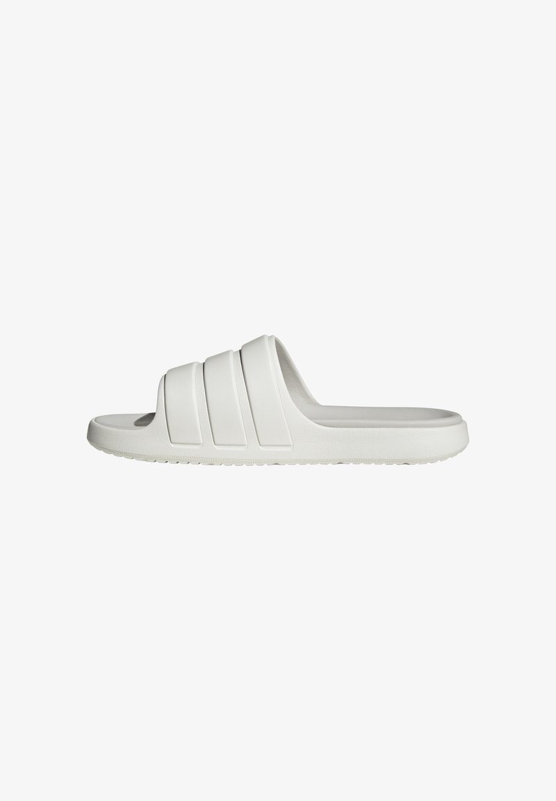 Sandalia blanca tipo slip-on hecha de goma suave, con tres franjas horizontales prominentes en la parte superior, que presenta una suela plana y una plantilla texturizada.