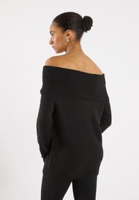 Pulover negru, cu umerii la vedere, din tricot cu textură cu nervuri, având mâneci lungi și o croială lejeră. Fără modele sau elemente metalice vizibile.