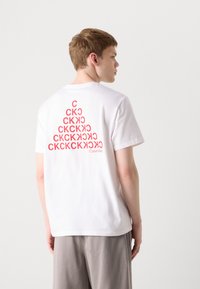 White cotton t-shirt featuring a red graphic design with letters on the back. Short sleeves and a crew neck with a relaxed fit.