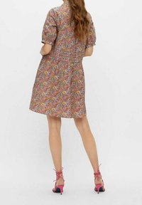 Sukienka w kwiatowy wzór z krótkimi bufkami, talią ściągniętą w pasie i rozkloszowanym dołem. Noszona z różowymi sandałami na obcasie z małym obcasem.