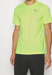 Camiseta atlética de manga corta en amarillo fluorescente, hecha de un material ligero. Presenta el logo de Puma en azul marino en el pecho.