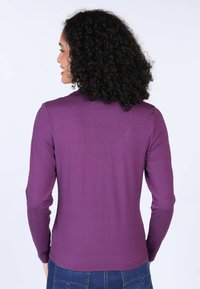 Long-sleeve shirt in deep purple, made from a soft fabric with a fitted design. Features a round neckline and subtle stitching details.