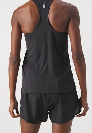 Atletisk person iført en sort racerback tanktop og sorte løbeshorts, stående med ryggen mod kameraet.