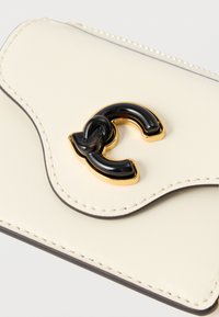 Kermaanse värinen nahkalompakko, jossa aaltoileva muotoilu, kullanväriset ja mustat korostusosat sekä eriväriset reunat. Sileä pinta ja ompeludetaljit.