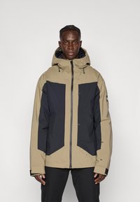 Μπεζ και ναυτικό μπουφάν με κουκούλα, διαθέτει εμπρόσθιο φερμουάρ, γωνιώδη σχεδιασμό και ελαστικά μανίκια. Κατασκευασμένο από υλικό με υφή, ανθεκτικό στις καιρικές συνθήκες.