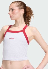 Szary, krótki top na ramiączkach w kolorze czerwonym z haftowanym logo "adidas". Miękki materiał, dopasowany krój i prosty, sportowy wygląd.