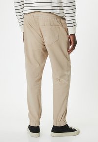 Beige byxor med elastisk midja och en något avsmalnande design, med en bakficka och ribbstickade muddar, kombinerat med svarta och vita sneakers.