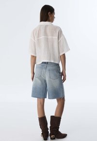 Maglietta a righe bianche a maniche corte, pantaloni corti in denim blu chiaro con una texture sbiadita e stivali fino al ginocchio marrone scuro con accessori decorativi.