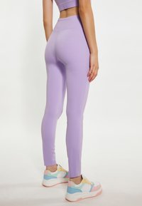 Leggings a vita alta color lilla con design aderente, caratterizzati da una texture liscia e dettagli delle cuciture, abbinati a sneakers multicolori.