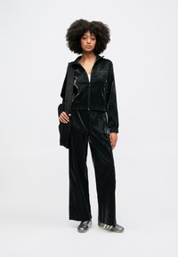 Juodas blizgus sportinis kostiumas su užtrauktuku ir elastinėmis kelnėmis. Priedai: bateliai su trimis juostelėmis ir juoda petneša.