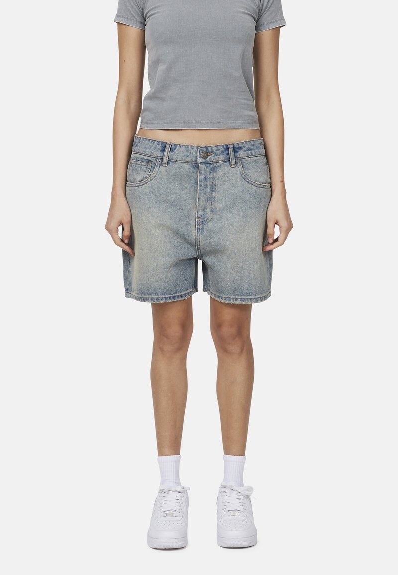 Jasnoniebieskie szorty dżinsowe o luźnym kroju, średnim stanie, pięć kieszeni i delikatne przetarcia. Połączone z dopasowaną szarością koszulą i białymi sneakersami.