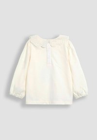 Cremfarbene Bluse mit langen Ärmeln und einem gezackten Ösenkragen, Knopfverschluss auf der Rückseite und gerafften Manschetten. Aus weichem Baumwollmaterial, schlichtes Design.