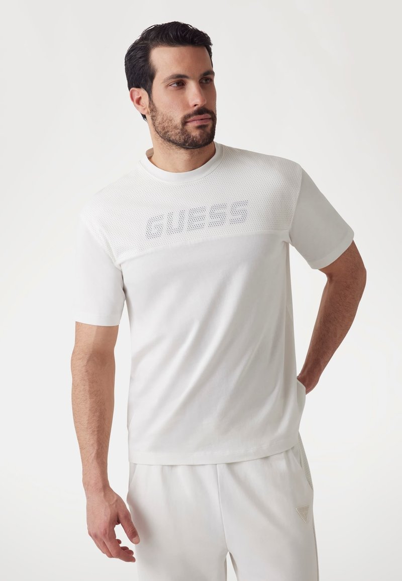 White short-sleeve t-shirt with mesh panel and "GUESS" logo across the chest. Soft fabric, relaxed fit, crew neck design.