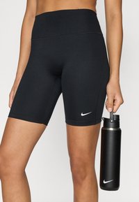 Μαύρο σορτς Nike με ψηλή μέση και λευκό λογότυπο Nike. Ένα μαύρο παγούρι κρατιέται σε ένα χέρι.