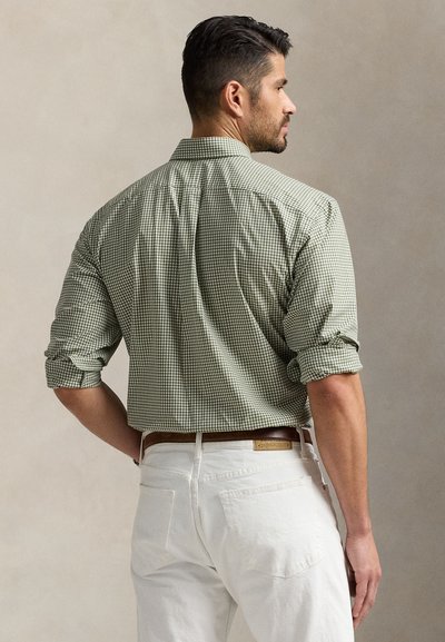 Πράσινο και λευκό καρό πουκάμισο με σηκωμένα μανίκια, φορεμένο με λευκά παντελόνια και καφέ ζώνη. Δείχνει την πίσω όψη και τις λεπτομέρειες του γιακά.