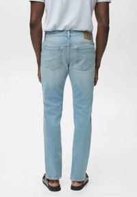Lichtblauwe denim jeans met een rechte snit, voorzien van twee achterzakken en een tan kleurige leren patch op de tailleband. De textuur lijkt glad.